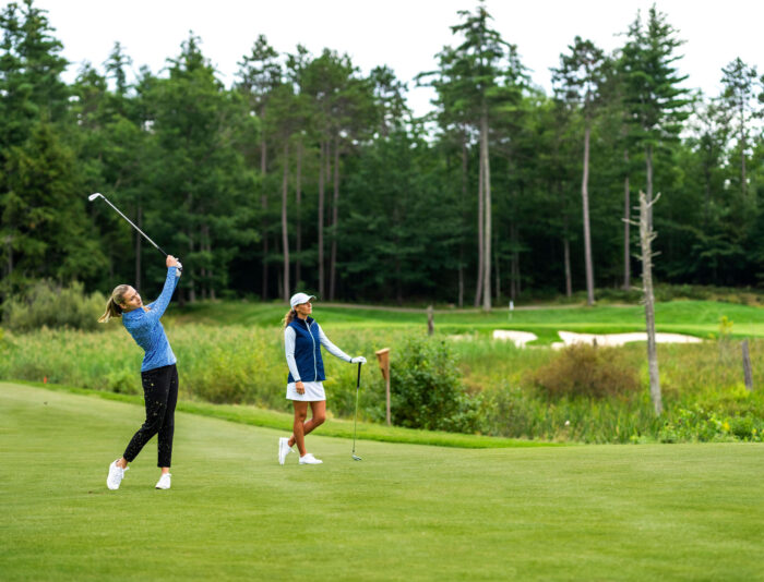 Two women golfers taking an iron shot on a fairway at Lake Winnipesaukee Golf Club.